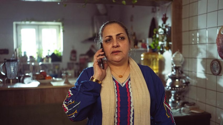 A middle-aged woman conversing on a phone in a cozy kitchen setting, portraying a domestic scene.